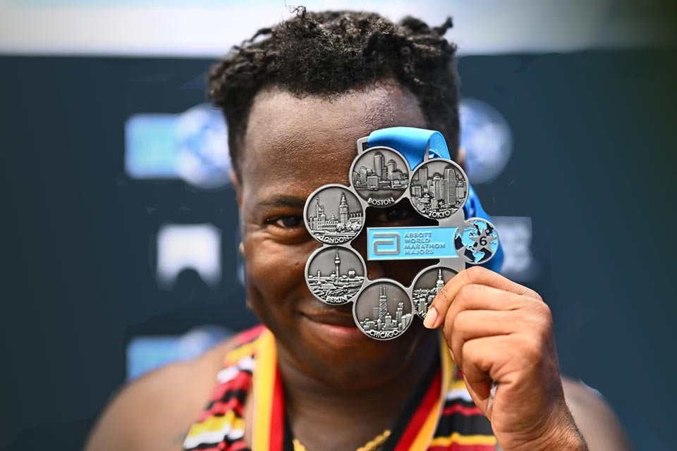 Cal State LA alumnus JT Chestnut holds up a World Marathon Majors medal in front of their face after completing the Abbott World Marathon series.