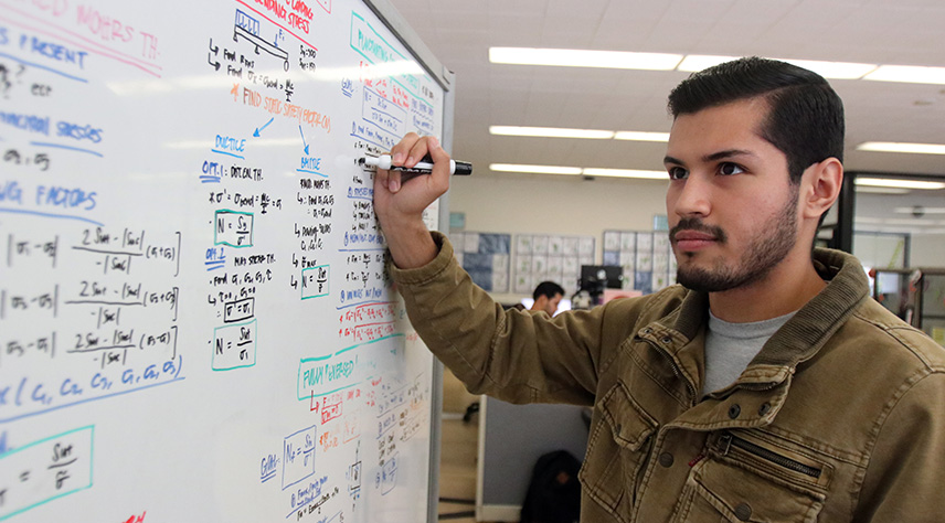 A male student writing on a dry erase board to solve a mathematic problem