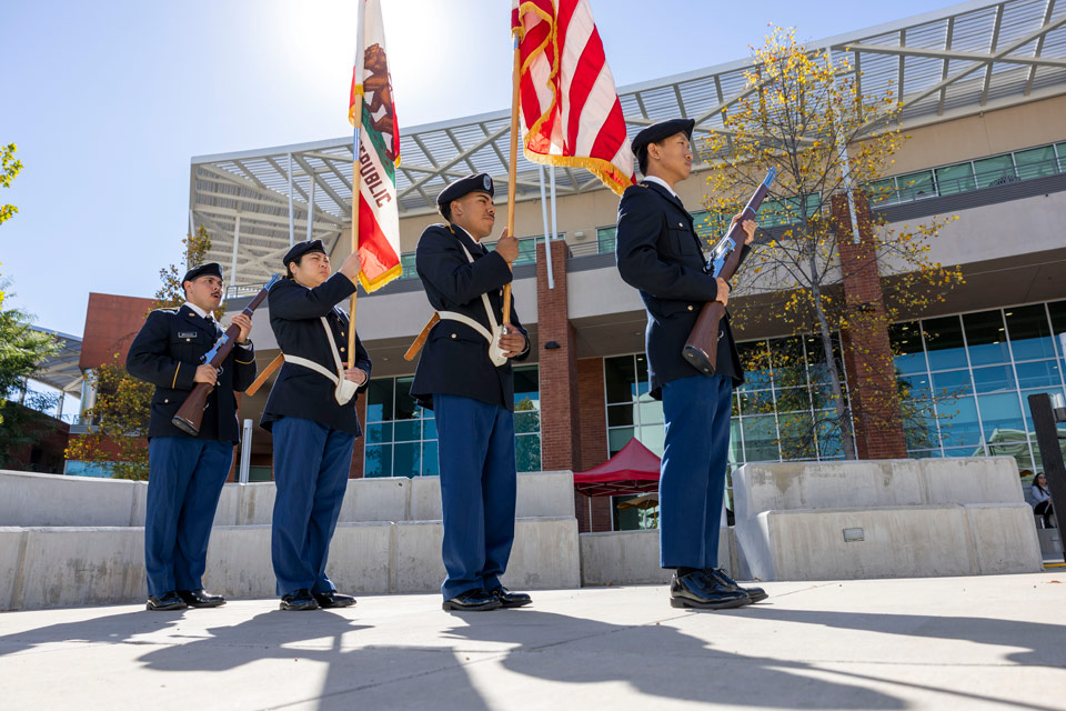 4 Veterans holding flags in front of a building on a sunny day.