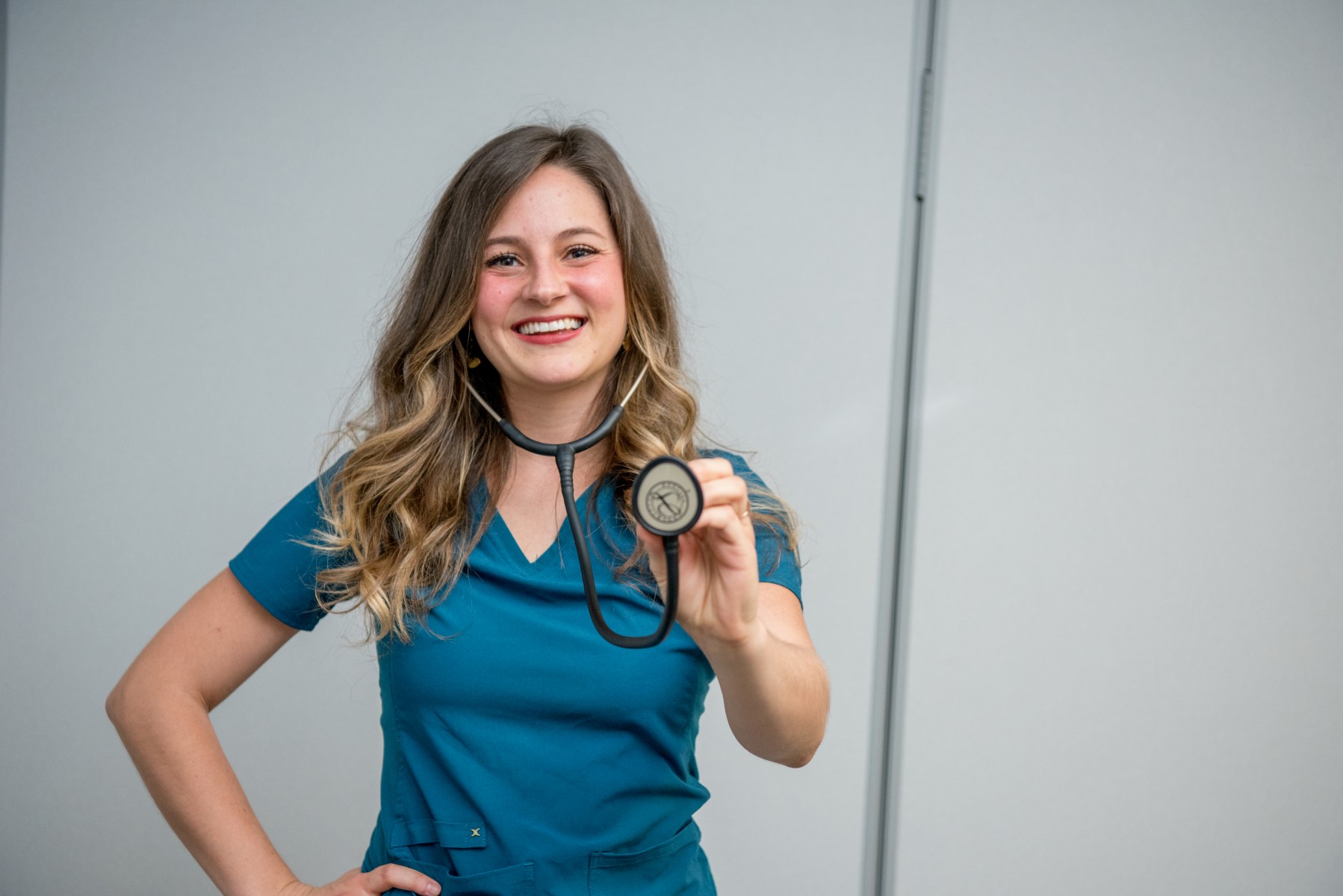 Nursing student Melody Henderson wears blue scrubs and smiles holding a stethoscope.