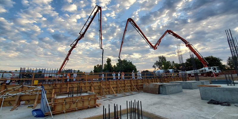 Constuction site with a building foundation. Orange cranes and various workers.