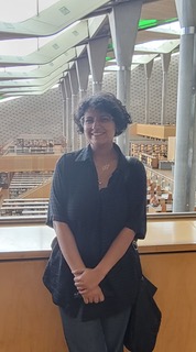 Woman with dark brown hair wearing a black dress shirt and dark grey dress pants