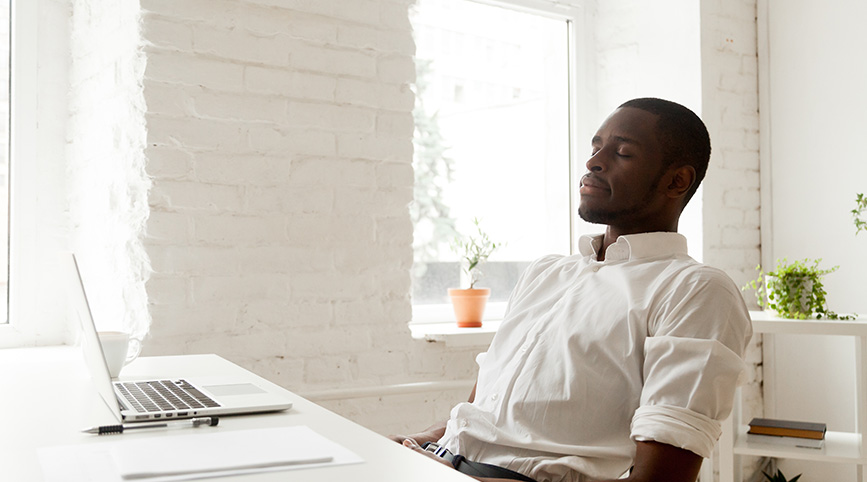 A black male meditating at his desk with his eyes closed.