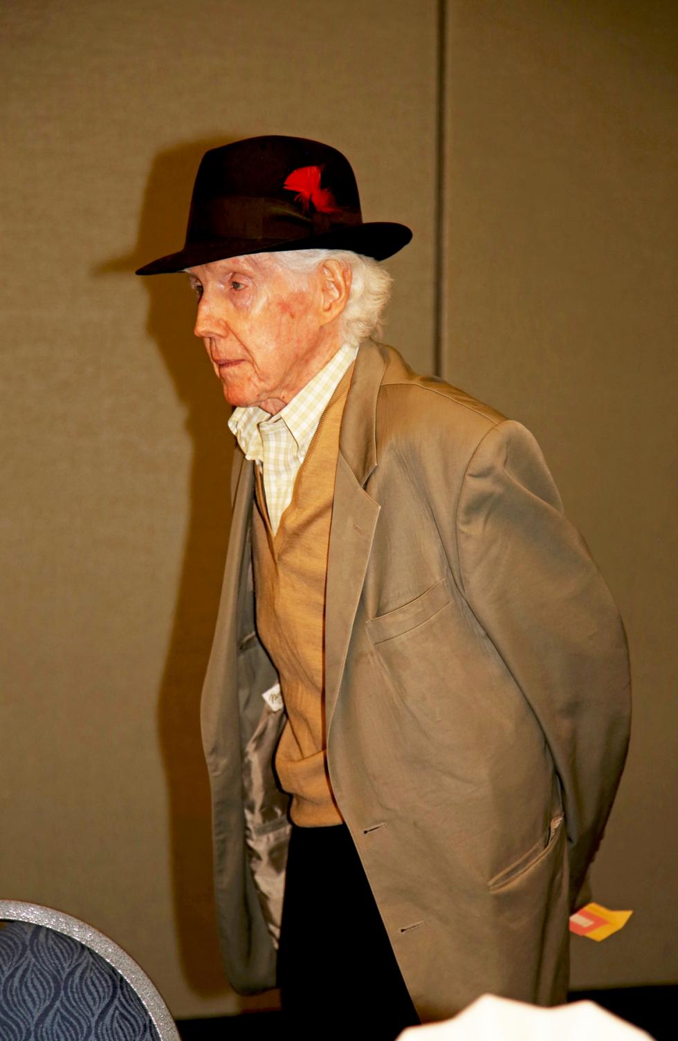 john wood; man in fedora hat with a red feather wearing a three piece suit