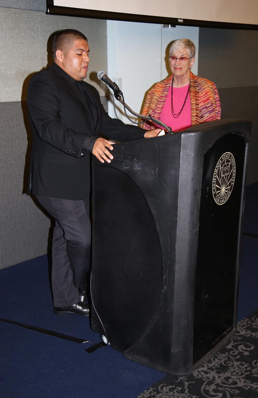 JosePerez, in business attire behind podium and using microphone