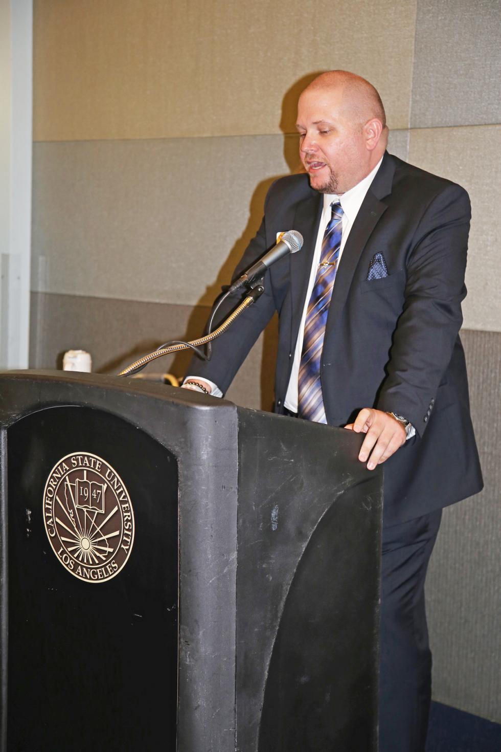 J,Steele, man wearing suit and tie,behind podium 