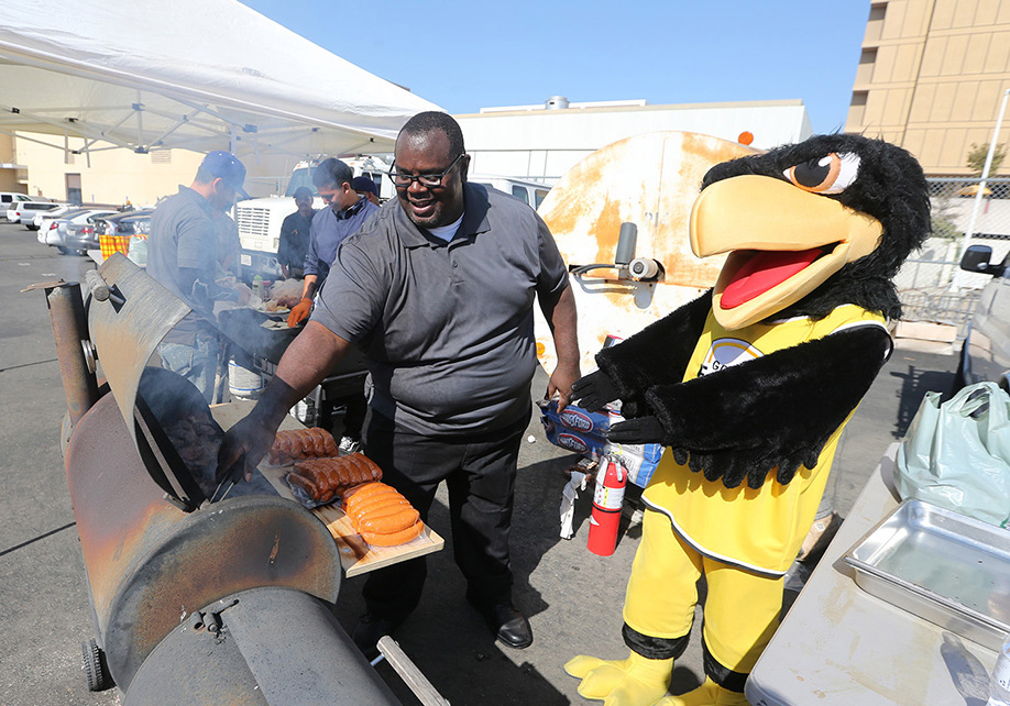 Old version of Eddie the Golden Eagle standing at a BBQ grill with a staff person.