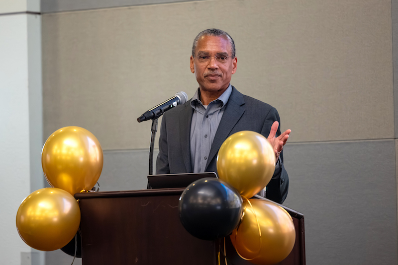 Dr. Stephen L. Mayo speaks at a podium during the Lloyd N. Ferguson Distinguished Lecture at Cal State LA, with gold and black balloons decorating the front.
