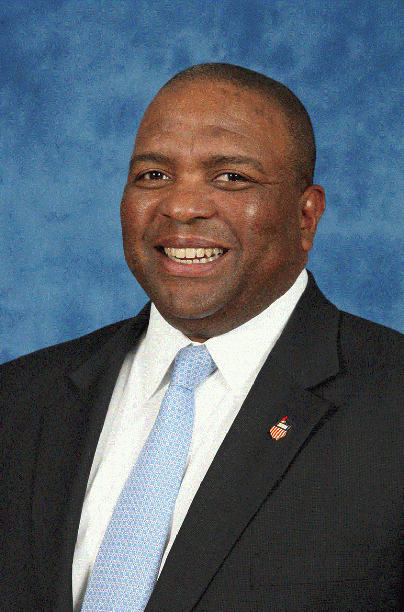 Headshot of Black man in black suit, white shirt and blue tie 