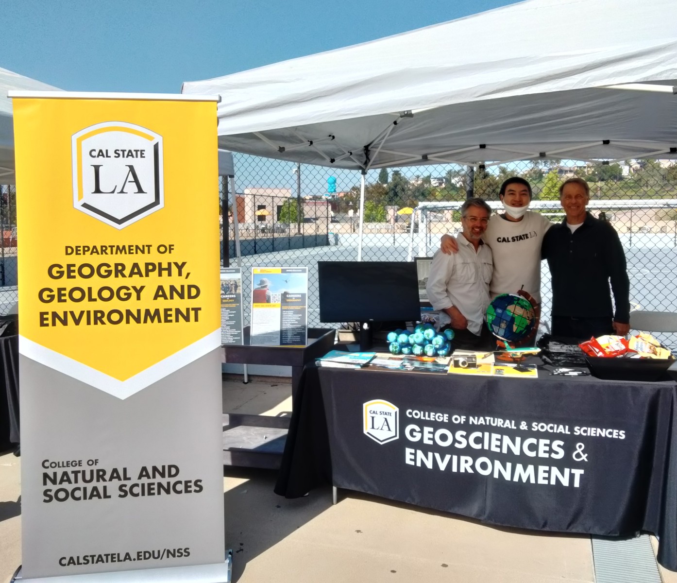 Three Staff standing in front of the GGE department infomation booth and banner. 