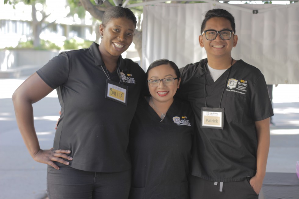 About Us- link page: Dalila, Jocelyn, and Patrick smiling as they pose for picture at community event