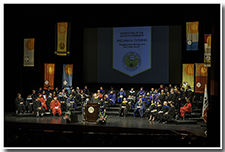 A wide picture of the platform party displays the academic regalia and colorful setting.