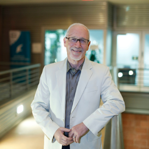 Man with white hair wearing black rimmed glasses and white jacket