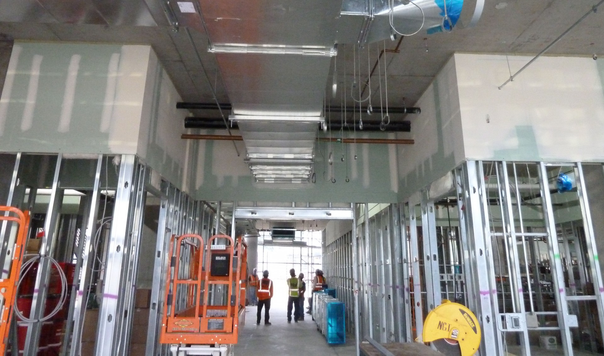 people in orange vests, metal beams visible in interior of building under construction