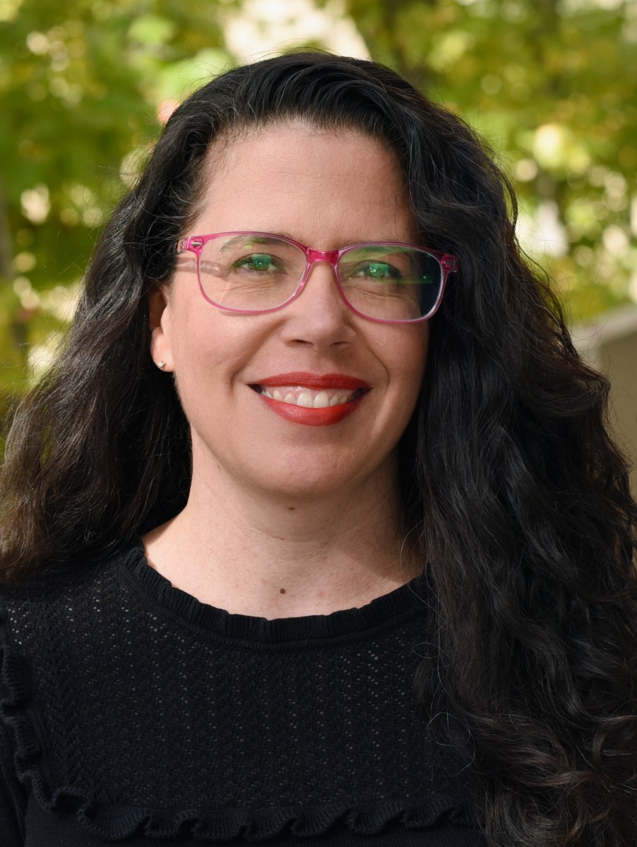 A person with long hair and glasses smiling.