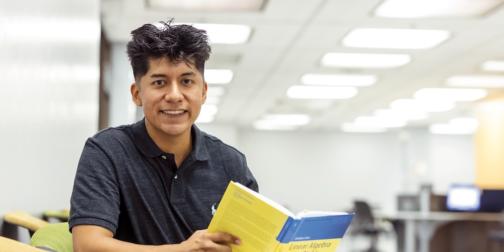 Yak de Padua wearing a black button up shirt reading a book