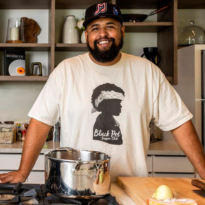Chef Martin Draluck standing behind a pot and stove smiling