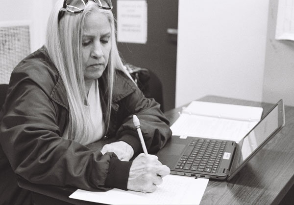 A PGI student writes on a sheet of paper while sitting at a desk. 