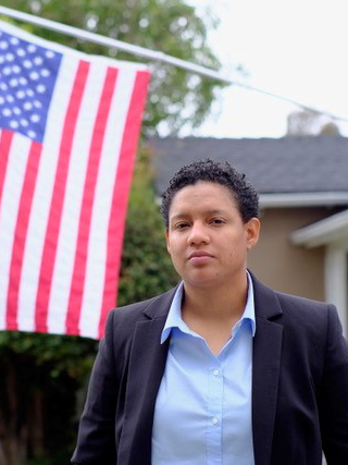 Itzel, wearing a blue shirt standing next to American flag