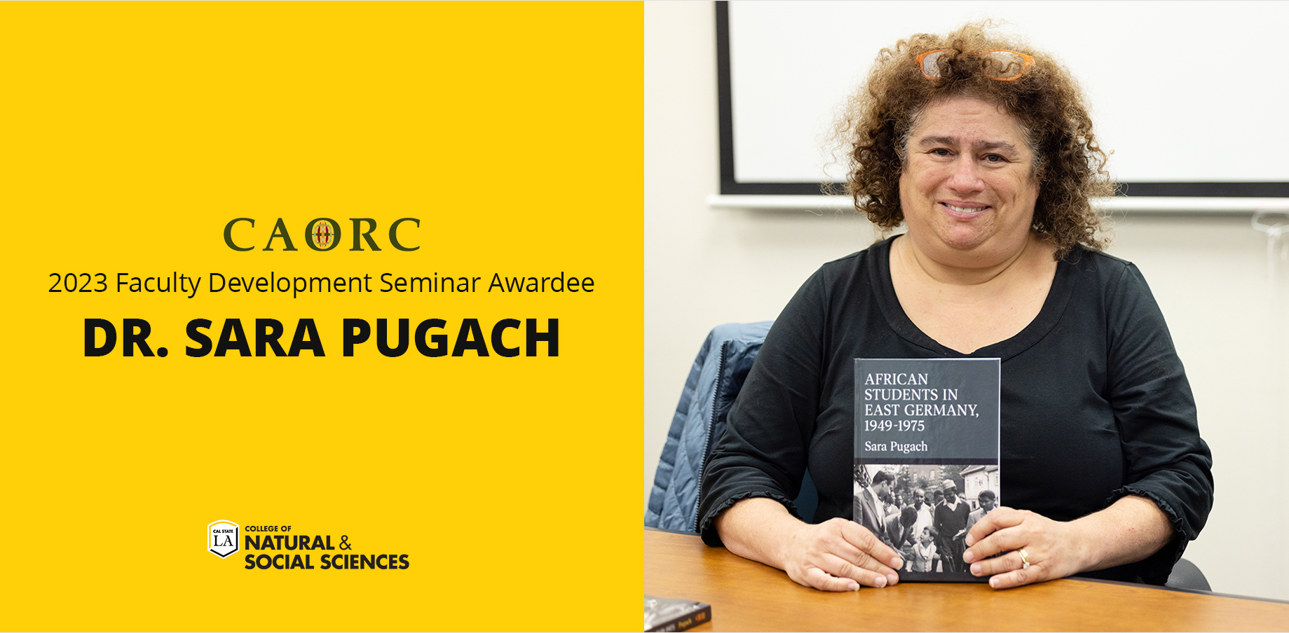 Dr. Sara Pugach sitting at a table holding up a book.