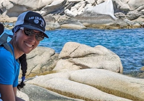 Amira wearing a baseball cap and sunglasses smiling while working out in the field
