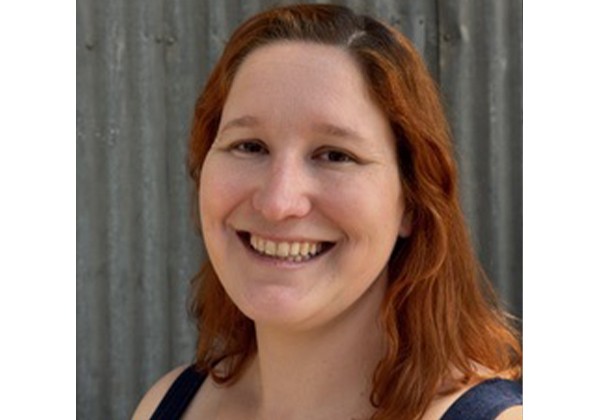 Portrait of Dr. Dear with red hair smiling in front of a grey background