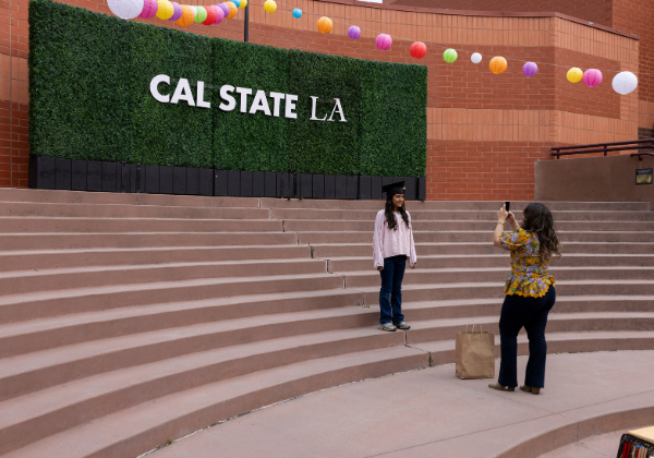 parent taking photo of child posing in front of hedges that say Cal State LA