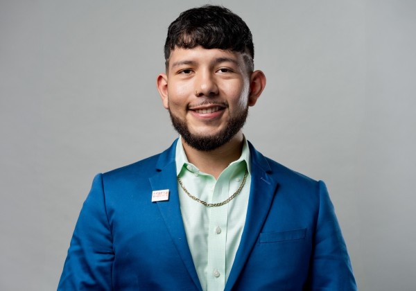 Portrait of Eder Perdomo Hernandez, CREAR Futuros mentor, smiling in a blue suit and light green shirt against a gray background.