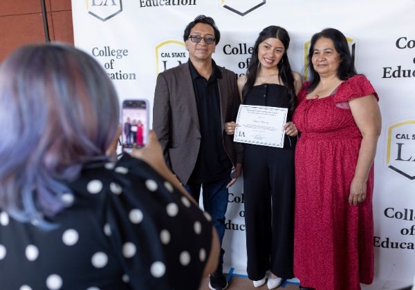 Family of three posing for photos in front of Cal State LA branded backdrop