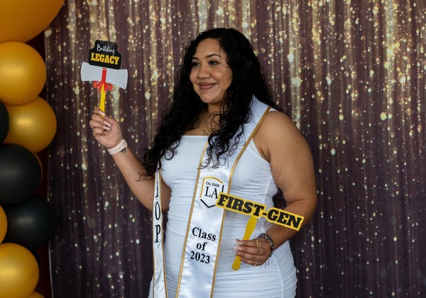 A person holding "First-Gen" and Building Legacy photo props while standing in front of a glittery curtain.
