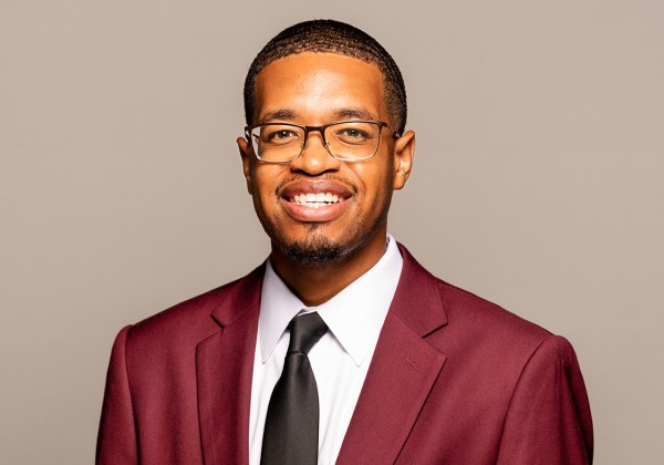 A person wearing glasses and a suit and tie smiling.