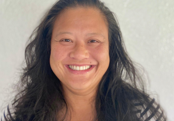 a person with a smiling expression, long hair and wearing a striped shirt