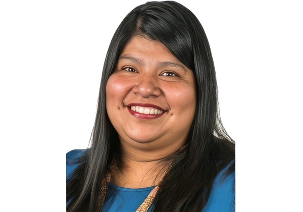 Lourdes smiling wearing a blue top standing in front of a white background.