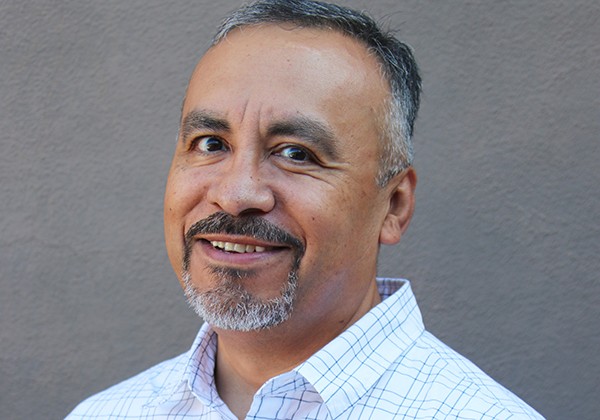 A person with salt-and-pepper facial hair smiling