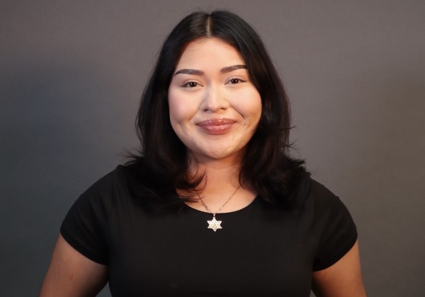 Portrait of Noemi Alanis, CREAR Futuros mentor, smiling in a black top with a star necklace against a dark gray background.