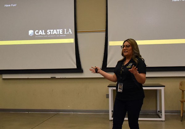 A person standing at the font of a lecture hall in front of two large screens.