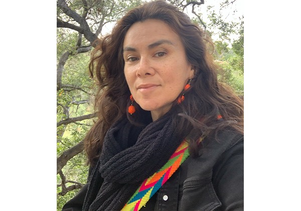 Olga Garcia sitting in front of trees wearing a black jacket and black scarf