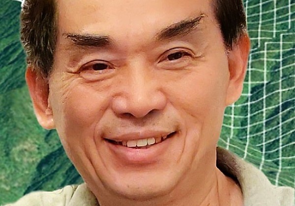 A man with light green shirt smiling with a Map GIS background.