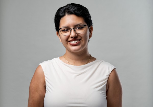 Portrait of Sam Aguilar, CREAR Futuros mentor, smiling in glasses and a white sleeveless top against a gray background.