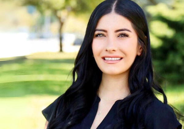 a person with long black hair smiling in front of trees