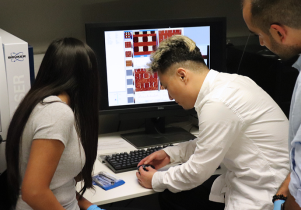 Dr Travis Hu isits in front of computer with students working in lab
