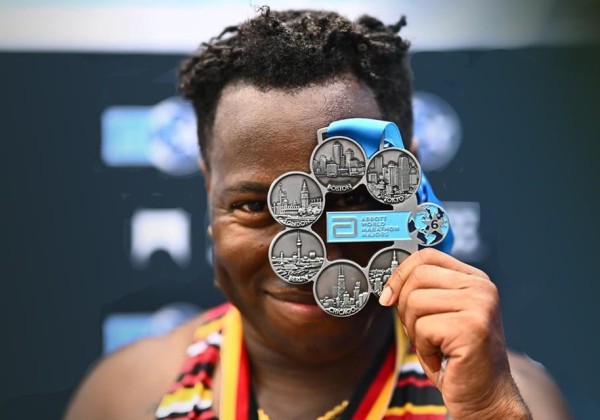 Cal State LA alumnus JT Chestnut holds up a World Marathon Majors medal in front of their face after completing the Abbott World Marathon series.