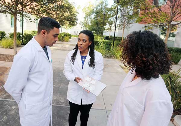 Professor Foster speaking to one male student and one female student wearing lab coats