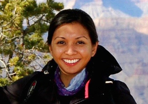 Lady with blackhair smiling at the camera stadning in front of Grand Canyon