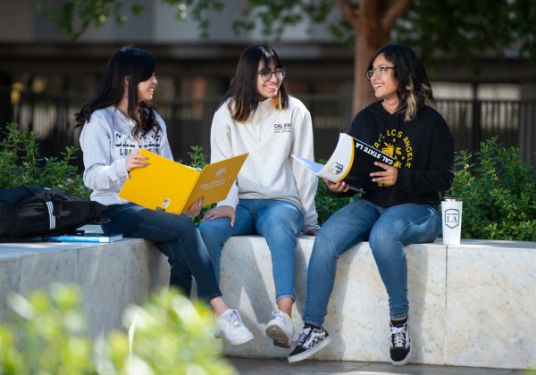 3 students sitting on a bench sharing notes