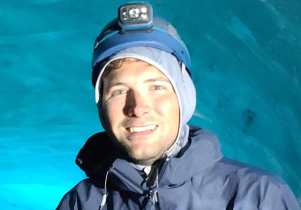 A man stand behind ice glaciers smiling.