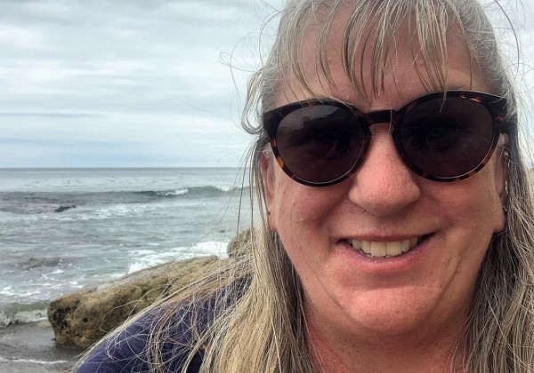 A woman at the beach wearing sunglasses and smiling.