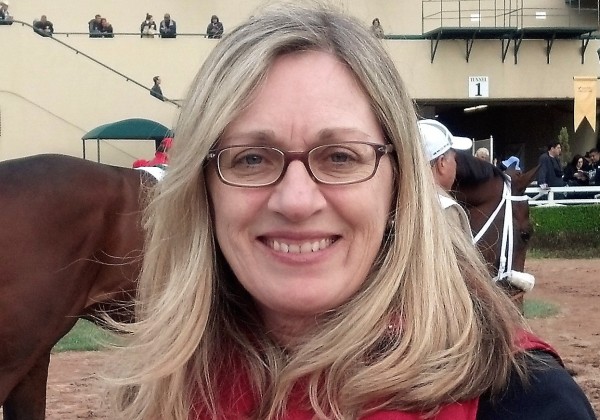 A woman at a horse track and smiling at the camera. 