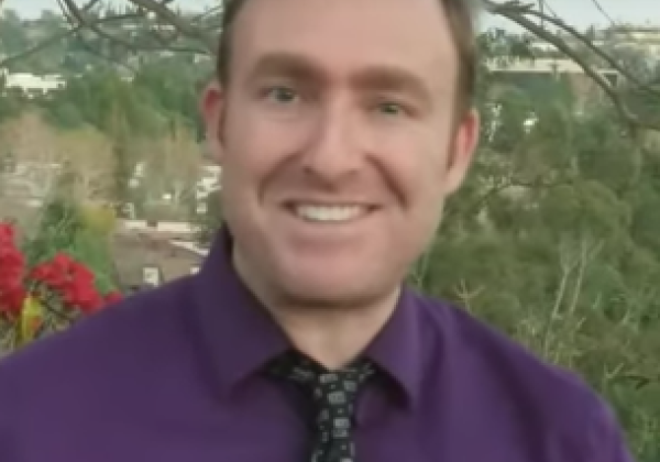 A man wear a purple shirt with a tie smiling.