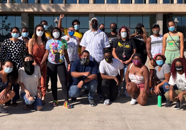 Large group of students wearing face coverings, outside on a sunny day.